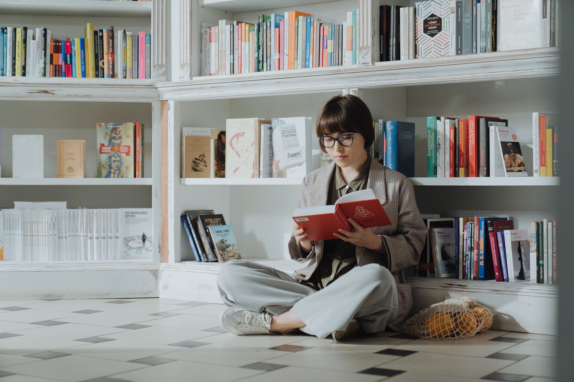 Image of a woman reading, in front of neatly arranged bookshelves.
